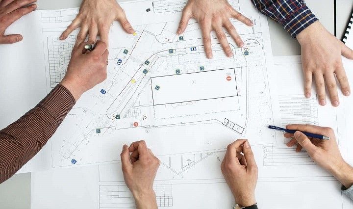 aerial view of Architects' hands, collaborating on a large building plan at a desk
